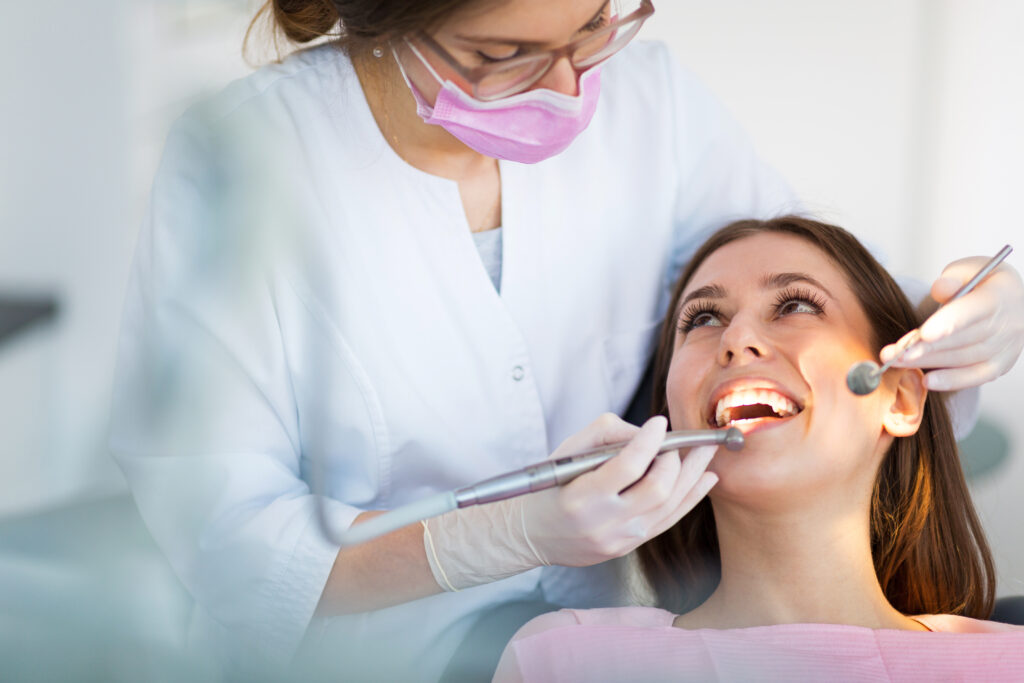 Woman sitting in dental chair looking up at dentist whilst smiling with clean, healthy teeth