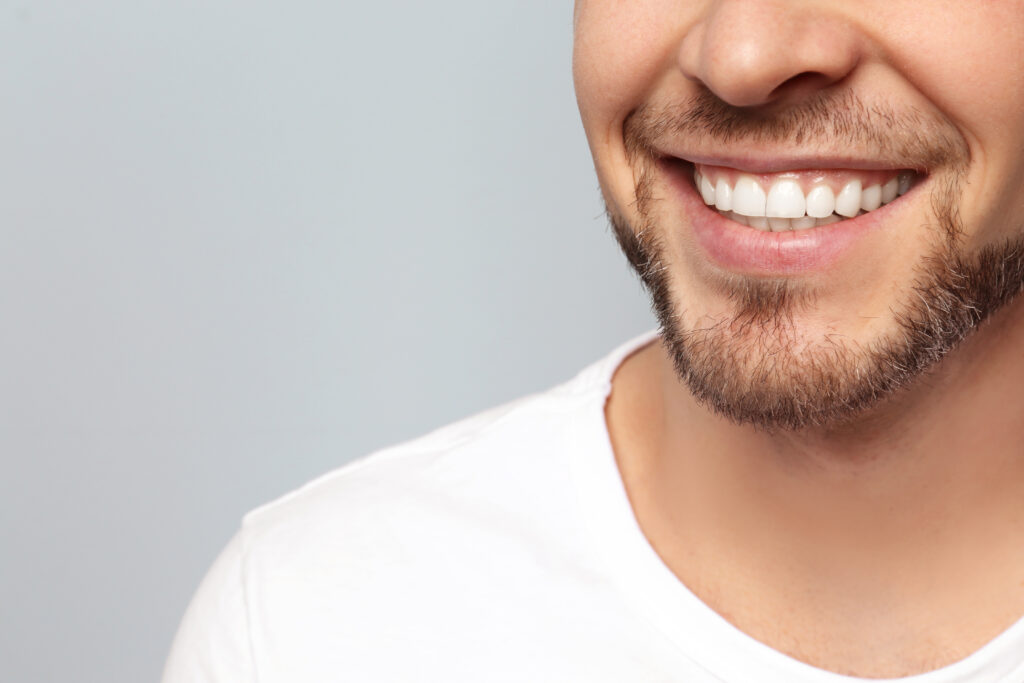 Young man with beautiful smile on grey background. Teeth straightening