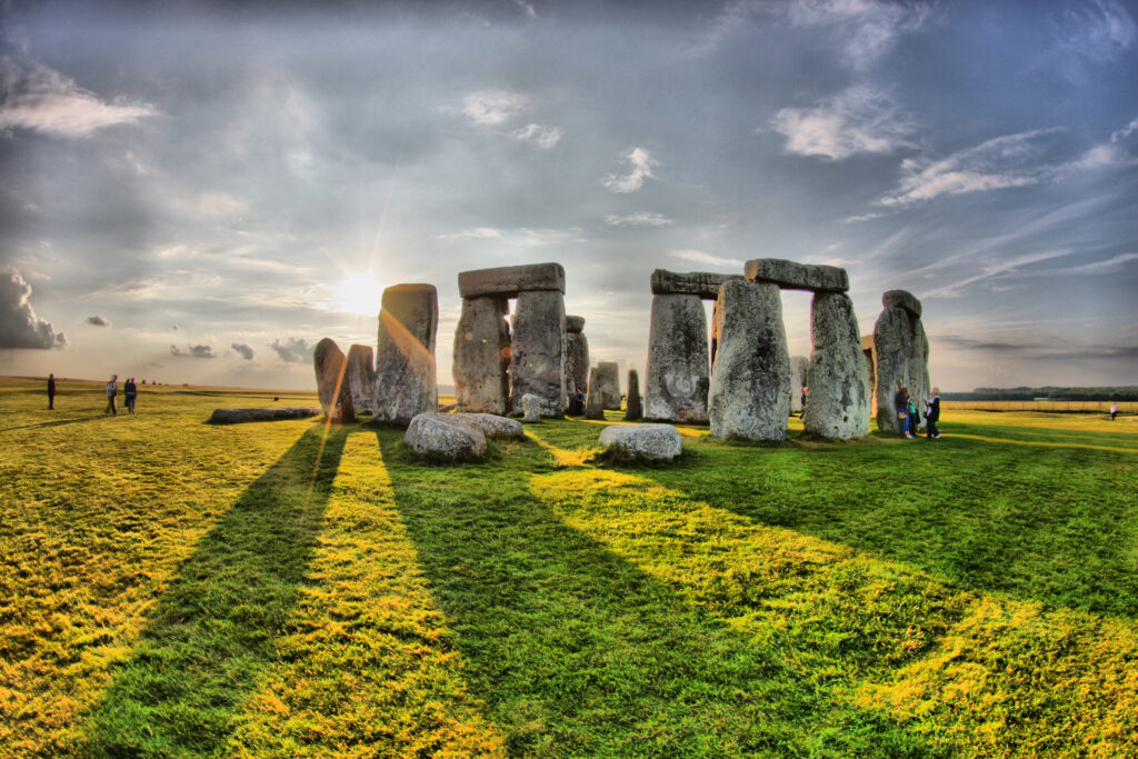 a photograph of Stonehenge from afar with the sun creeping through the rocks