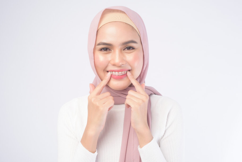 A young muslim woman holding colorful retainer for teeth over white background studio.